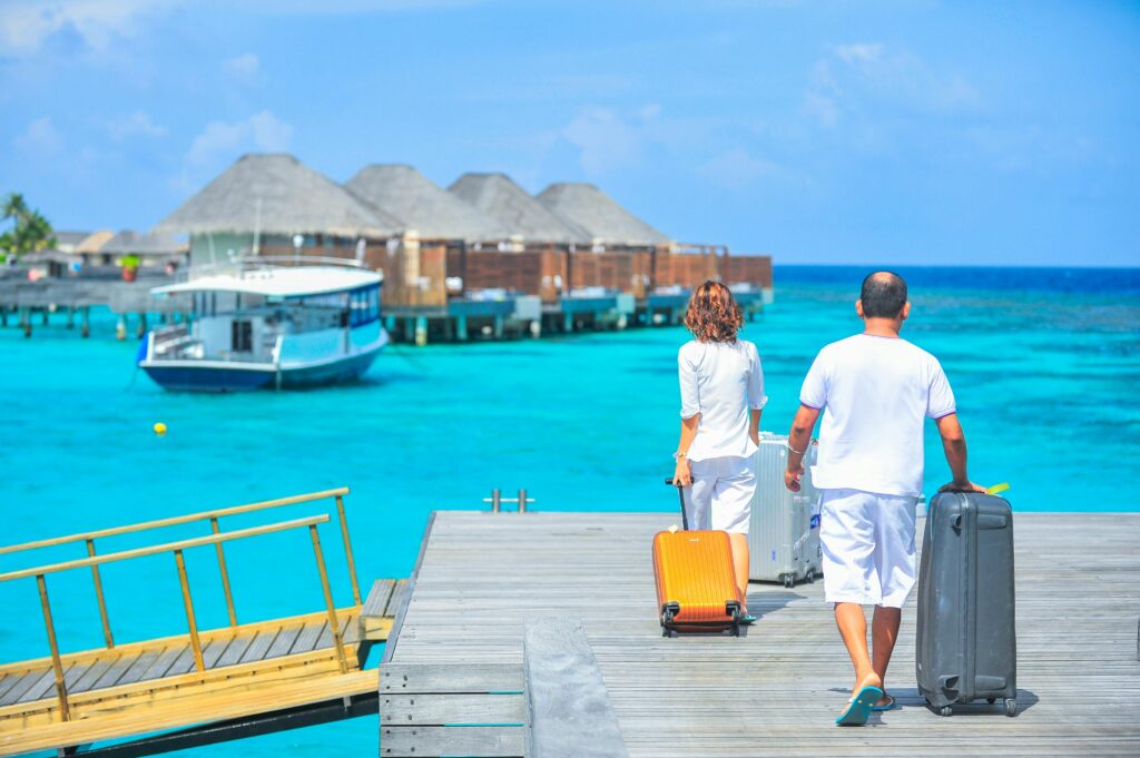 A couple with suitcases walks down a wooden pier towards luxury overwater bungalows, representing the dream vacation you can plan with the help of our timeshare cost per point calculator.