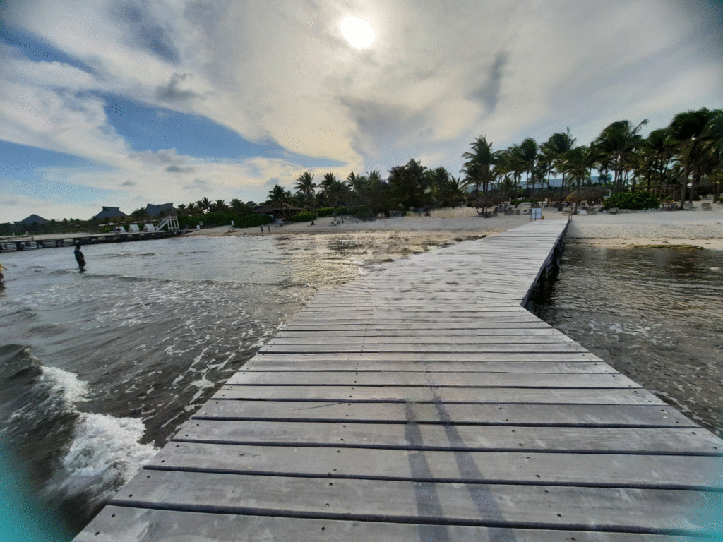 Wooden pier to a calm, palm-lined beach in Cozumel at sunset—easy access and shallow water for families.