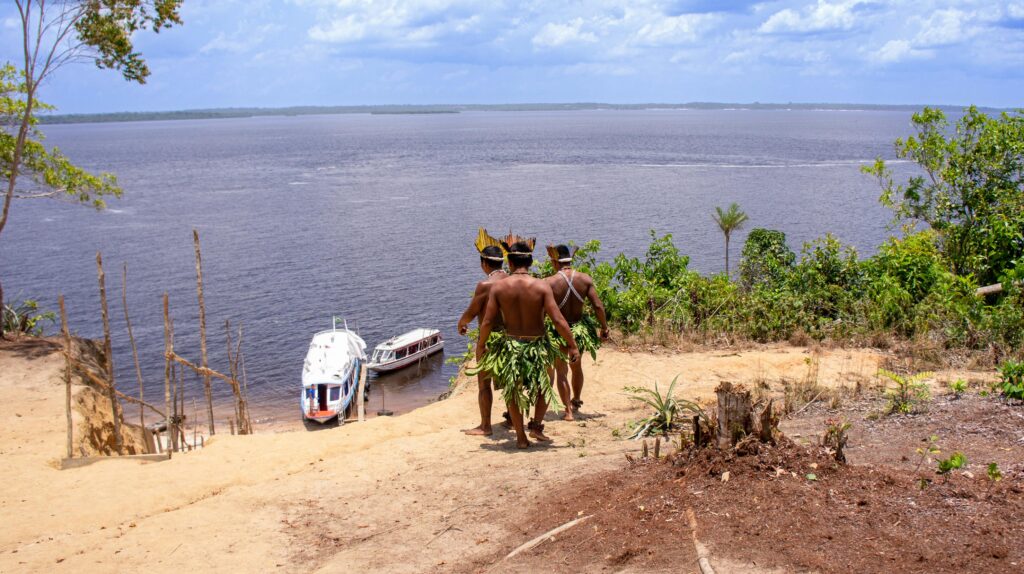 Indigenous guides in traditional attire walking toward river boats above the Amazon near Manaus, Brazil